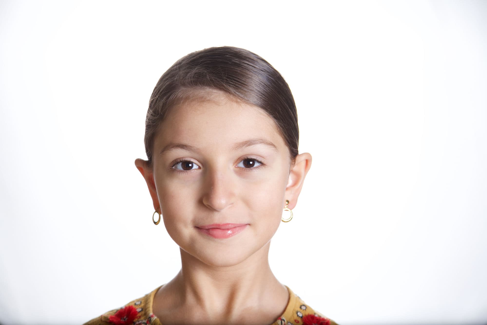 Portrait of a smiling young girl with gold hoop earrings on a white background