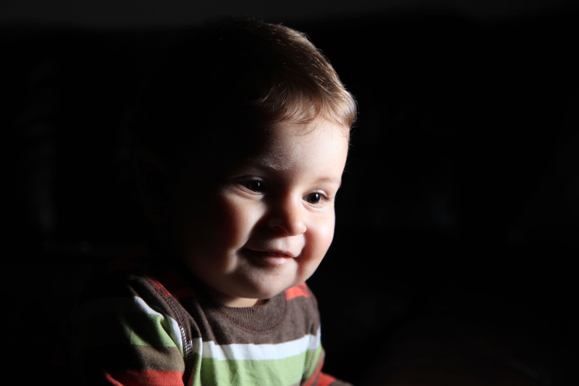 Low-key portrait of a smiling toddler in a striped top against a black background