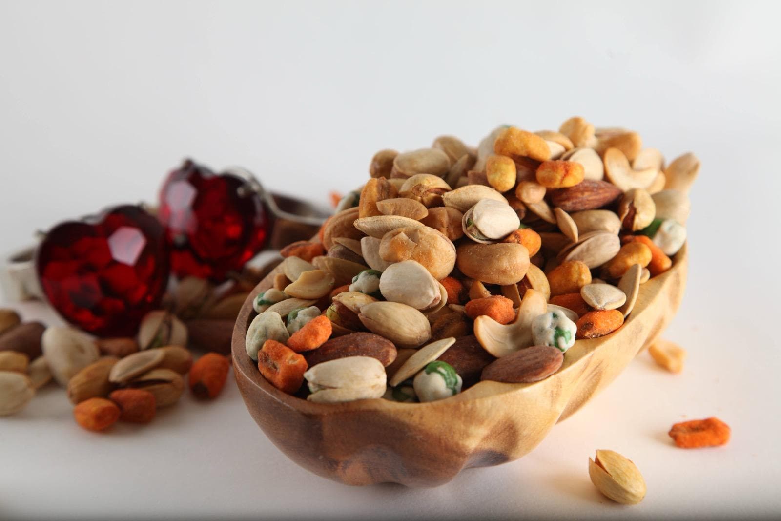 Food product photography of mixed nuts in a wooden bowl with red crystal props on a white background